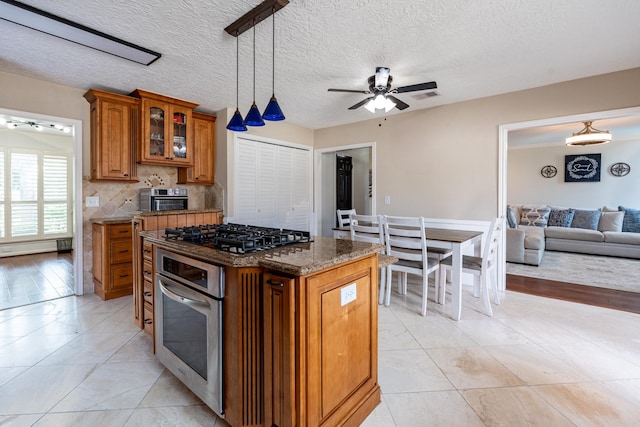 kitchen with black gas cooktop, glass insert cabinets, brown cabinetry, oven, and a ceiling fan