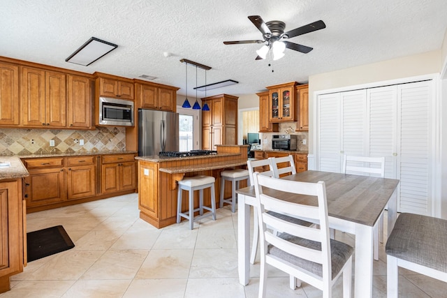 kitchen with brown cabinets, stainless steel appliances, ceiling fan, tasteful backsplash, and a center island