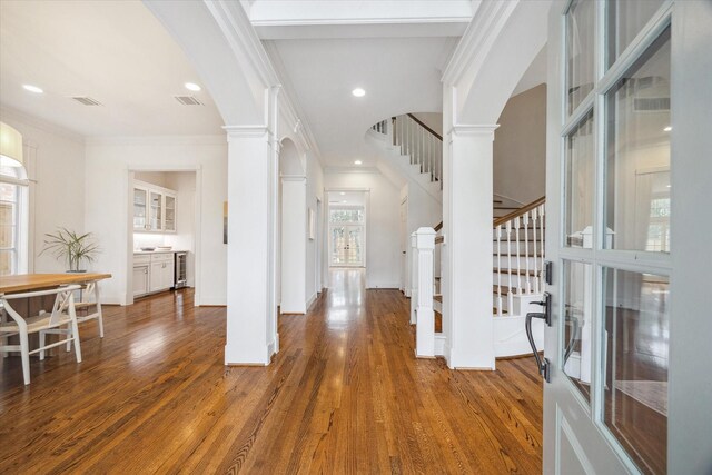 foyer with arched walkways, crown molding, and decorative columns
