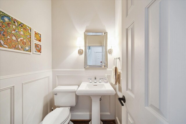 bathroom with a decorative wall, toilet, and a wainscoted wall