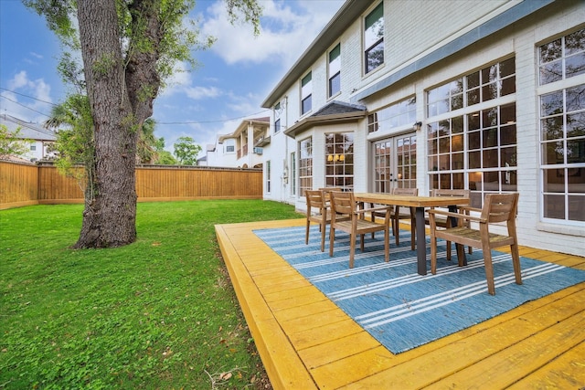 deck featuring a fenced backyard, a yard, outdoor dining space, and french doors