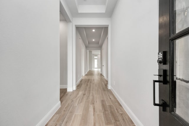 corridor with baseboards, a tray ceiling, recessed lighting, and light wood-style flooring