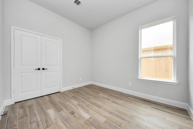 spare room with light wood finished floors, visible vents, and baseboards
