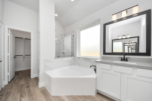 bathroom with vaulted ceiling, walk in shower, a garden tub, vanity, and wood finished floors