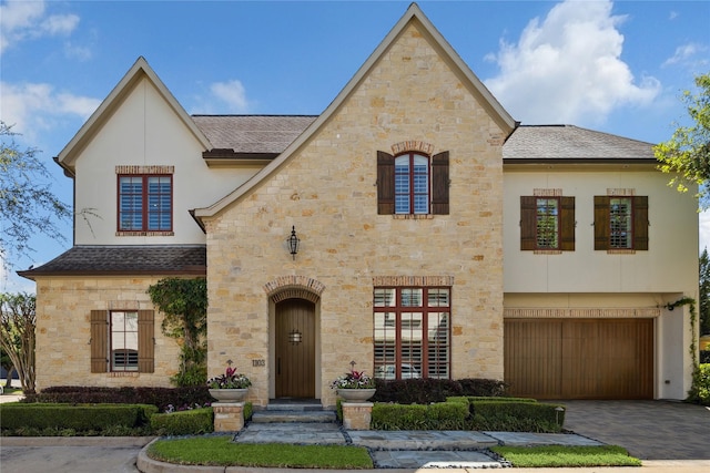 view of front of home with a garage, stone siding, stucco siding, a shingled roof, and driveway