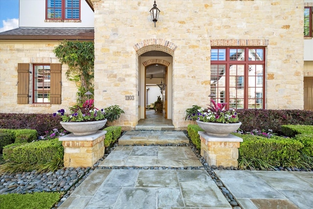 view of exterior entry with roof with shingles and stone siding