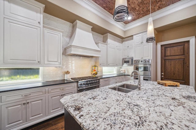 kitchen featuring crown molding, white cabinetry, custom range hood, a sink, and stainless steel appliances