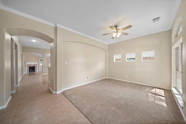 carpeted spare room featuring baseboards, ornamental molding, ceiling fan, and arched walkways