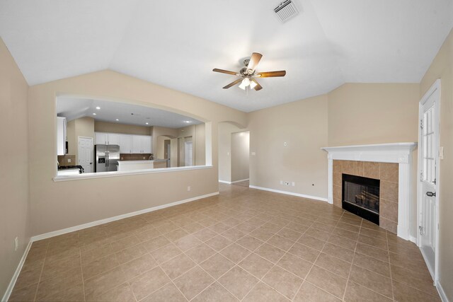unfurnished living room with a tile fireplace, light tile patterned floors, vaulted ceiling, visible vents, and a ceiling fan