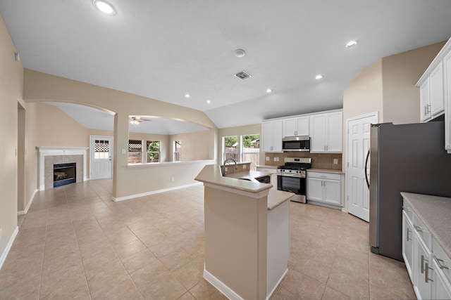 kitchen featuring a tile fireplace, stainless steel appliances, visible vents, backsplash, and lofted ceiling