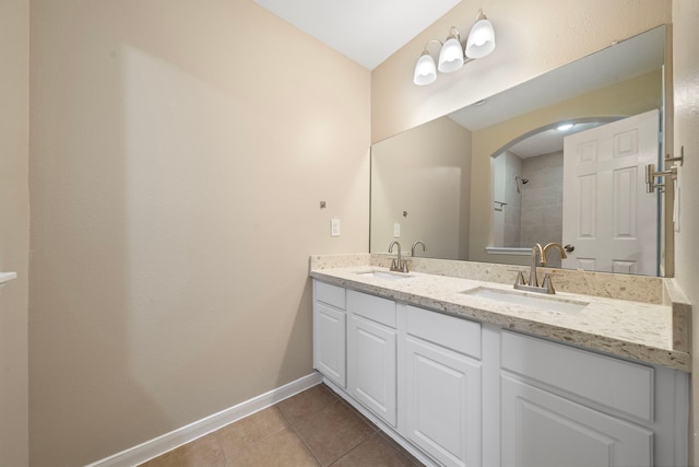 bathroom with double vanity, a sink, tile patterned floors, and baseboards