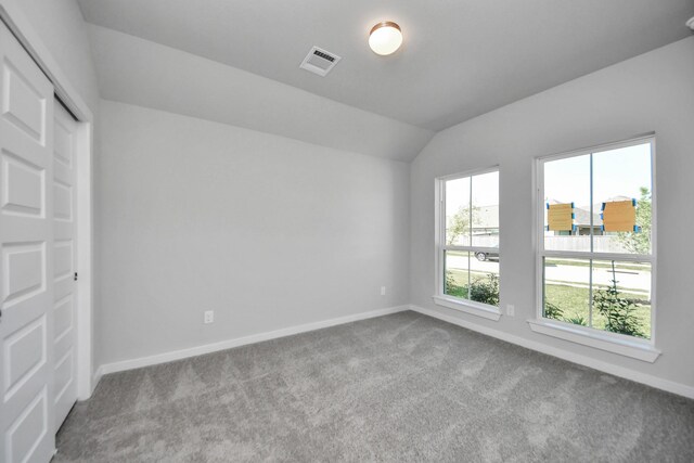 carpeted empty room with baseboards, lofted ceiling, and visible vents