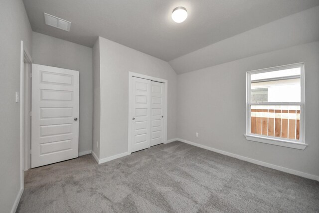 unfurnished bedroom featuring baseboards, visible vents, carpet, lofted ceiling, and a closet