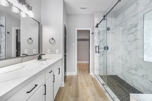 full bath with a spacious closet, wood finished floors, and a marble finish shower