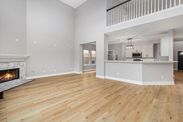 unfurnished living room with light wood-type flooring, a premium fireplace, baseboards, and high vaulted ceiling
