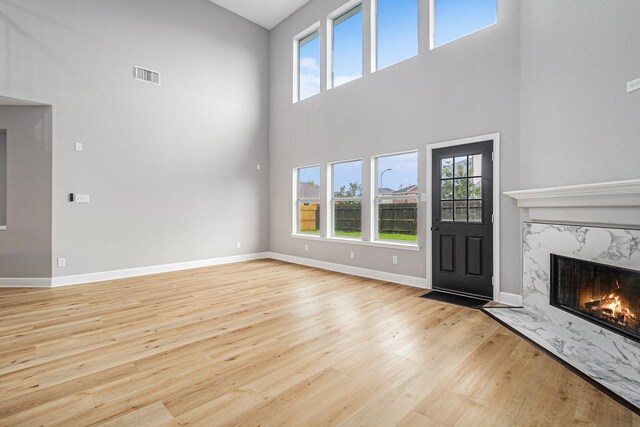 unfurnished living room with a towering ceiling, wood finished floors, visible vents, baseboards, and a fireplace
