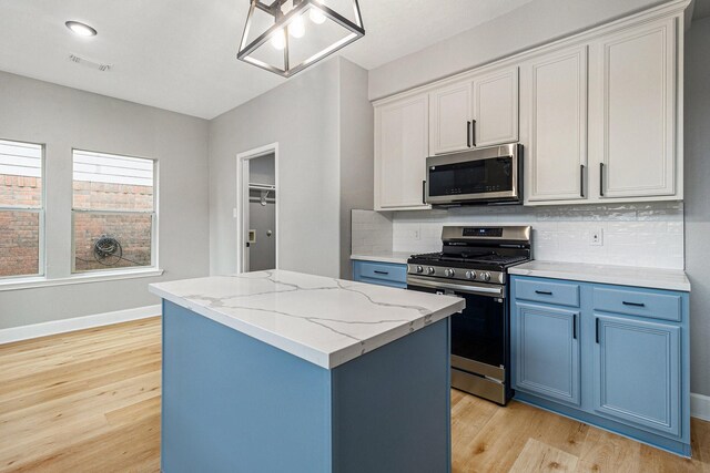 kitchen featuring stainless steel appliances, blue cabinets, light wood-type flooring, a kitchen island, and decorative backsplash