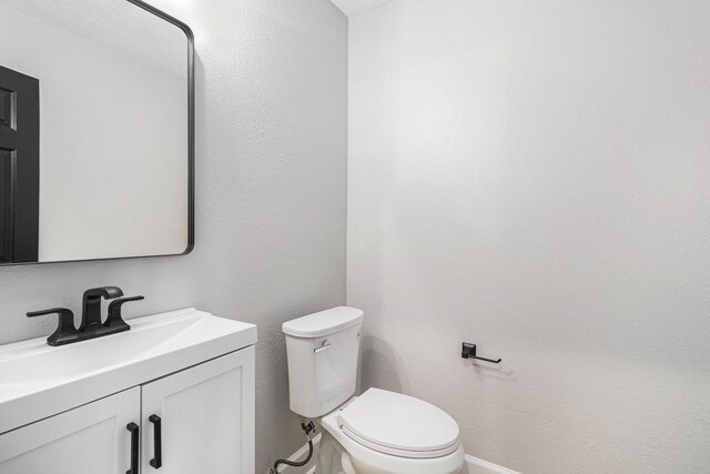 half bath with baseboards, vanity, and toilet