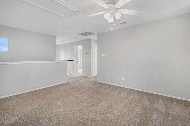 carpeted empty room with attic access, ceiling fan, baseboards, and visible vents