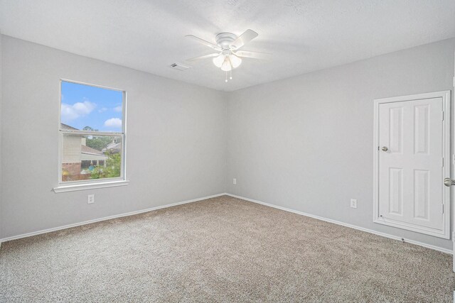 carpeted empty room featuring visible vents, a ceiling fan, and baseboards