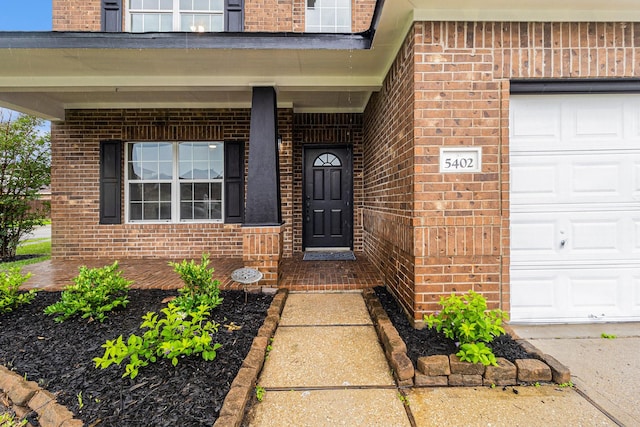 entrance to property with brick siding, covered porch, and a garage