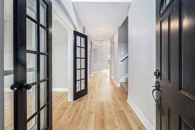 foyer entrance featuring stairs, light wood finished floors, baseboards, and french doors