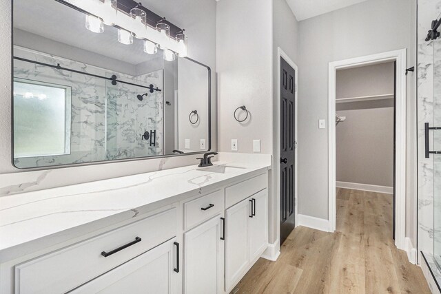 bathroom featuring wood finished floors, vanity, a marble finish shower, a walk in closet, and baseboards