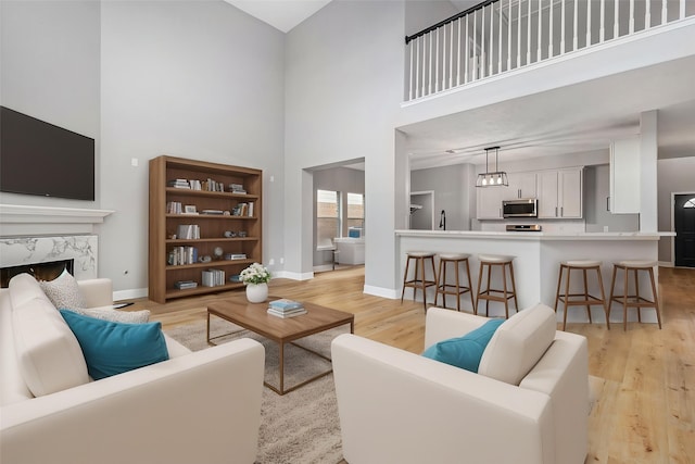 living area with a fireplace, a high ceiling, light wood finished floors, and baseboards