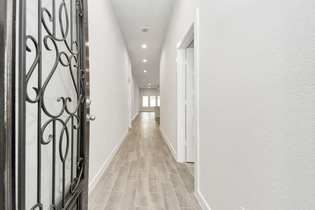 hall featuring light wood finished floors, baseboards, visible vents, and recessed lighting
