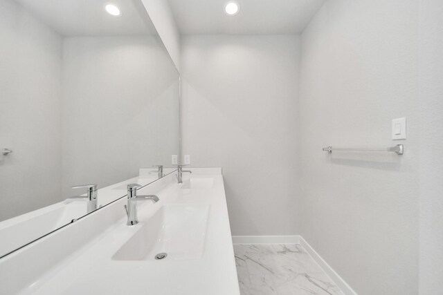 bathroom with marble finish floor, baseboards, a sink, and double vanity