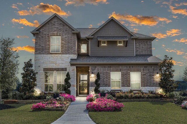 view of front of home with brick siding, stone siding, a shingled roof, and a front yard