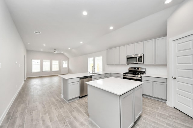 kitchen with a sink, open floor plan, light wood-style flooring, lofted ceiling, and appliances with stainless steel finishes