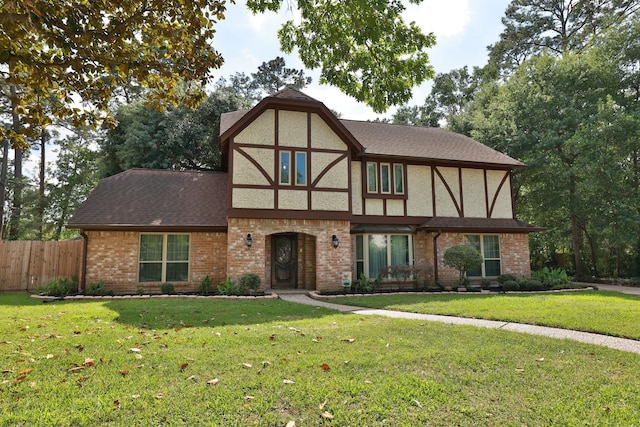 tudor home with fence, a front lawn, brick siding, and roof with shingles