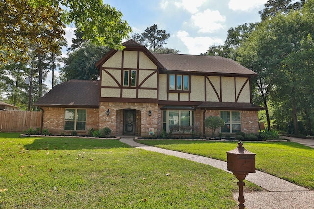 tudor house with fence, a front lawn, brick siding, and stucco siding