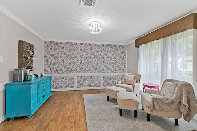 sitting room with wallpapered walls, visible vents, ornamental molding, light wood-type flooring, and a chandelier