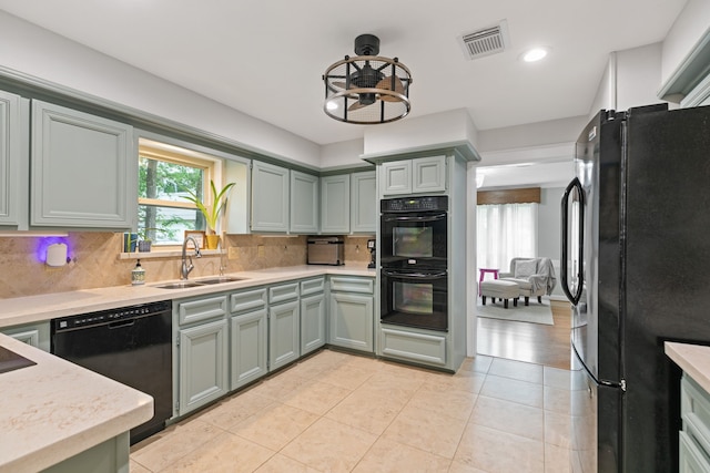 kitchen featuring a sink, black appliances, light tile patterned floors, backsplash, and visible vents