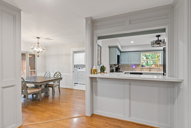 kitchen with light countertops, backsplash, washing machine and clothes dryer, light wood-style flooring, and a notable chandelier