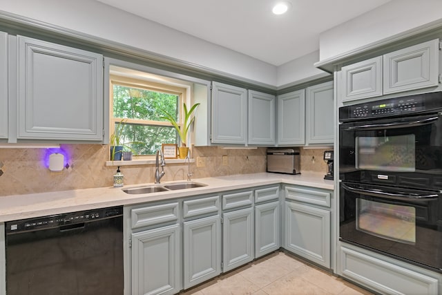 kitchen featuring a sink, tasteful backsplash, black appliances, light countertops, and light tile patterned floors
