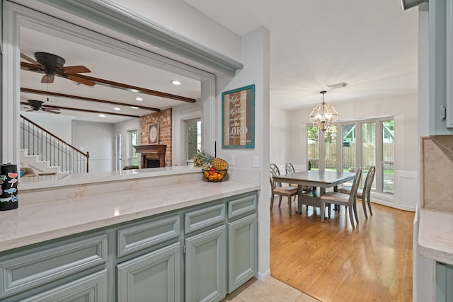 kitchen with ceiling fan with notable chandelier, a fireplace, light stone countertops, beam ceiling, and visible vents