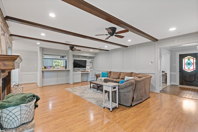 living area with a fireplace with raised hearth, light wood-style floors, a decorative wall, and ceiling fan