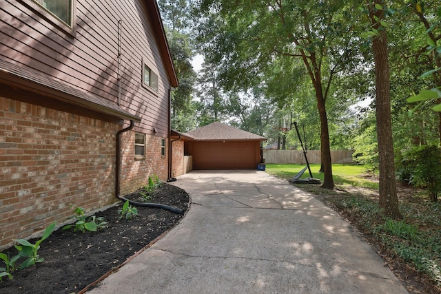 view of home's exterior featuring brick siding, an attached garage, driveway, and fence