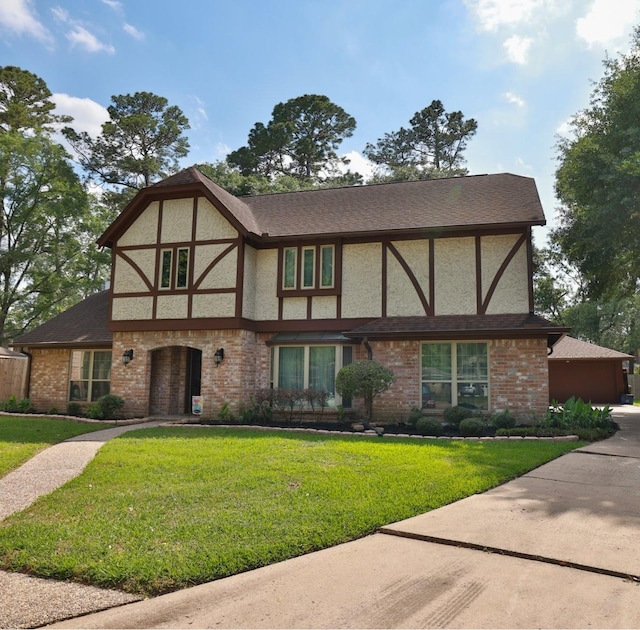 tudor home featuring stucco siding, brick siding, and a front yard