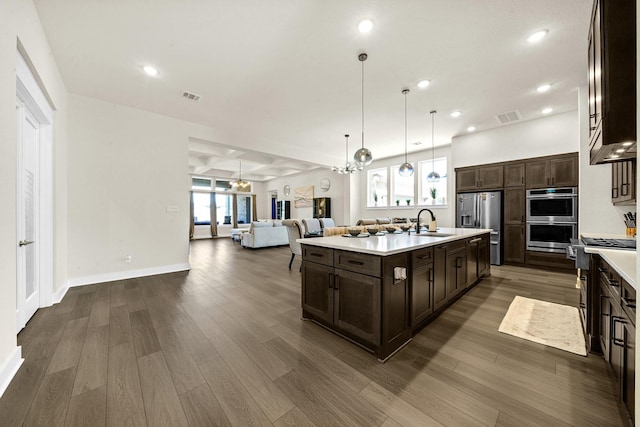 kitchen featuring dark brown cabinetry, visible vents, a sink, open floor plan, and stainless steel appliances