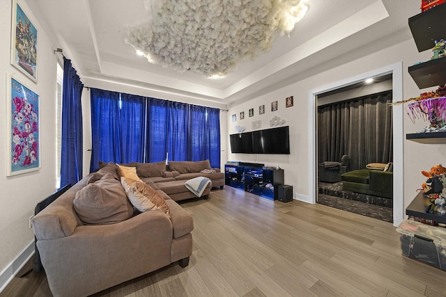 living area with baseboards, a tray ceiling, and wood finished floors
