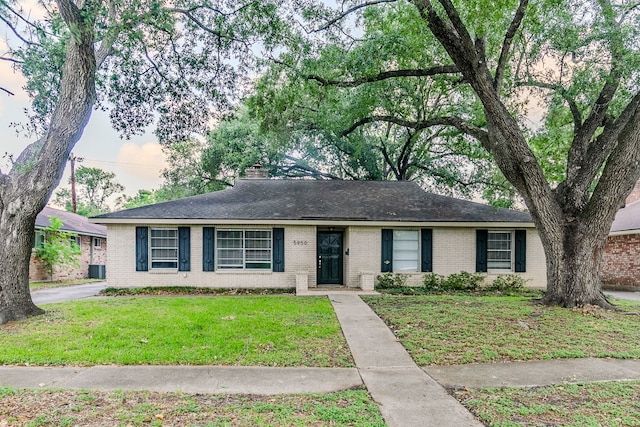 single story home featuring brick siding, a chimney, and a front yard