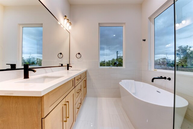 bathroom featuring tile walls, double vanity, a sink, and a freestanding bath