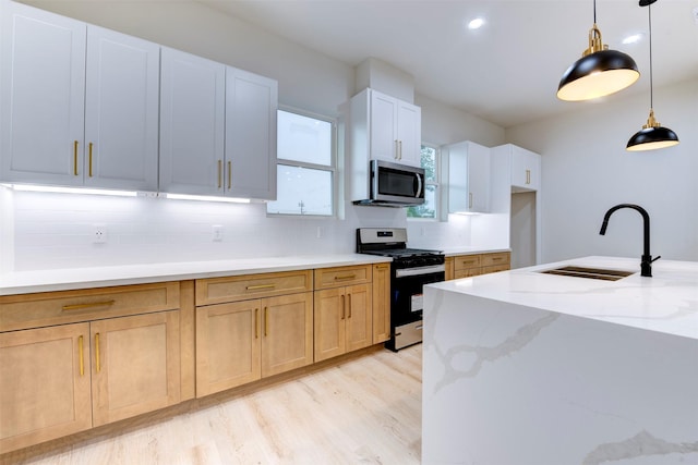 kitchen with backsplash, a sink, decorative light fixtures, light stone countertops, and appliances with stainless steel finishes