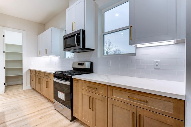 kitchen with decorative backsplash, light wood finished floors, light countertops, white cabinets, and appliances with stainless steel finishes