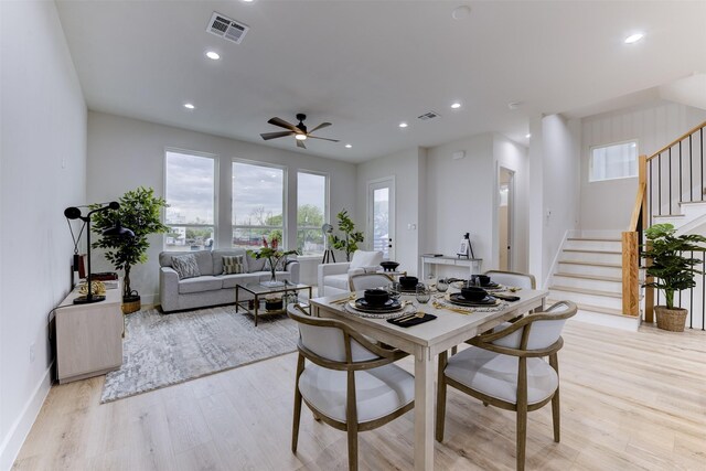 dining room featuring light wood finished floors, a ceiling fan, visible vents, and stairs