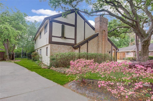 view of side of home with a chimney, fence, a yard, stucco siding, and brick siding